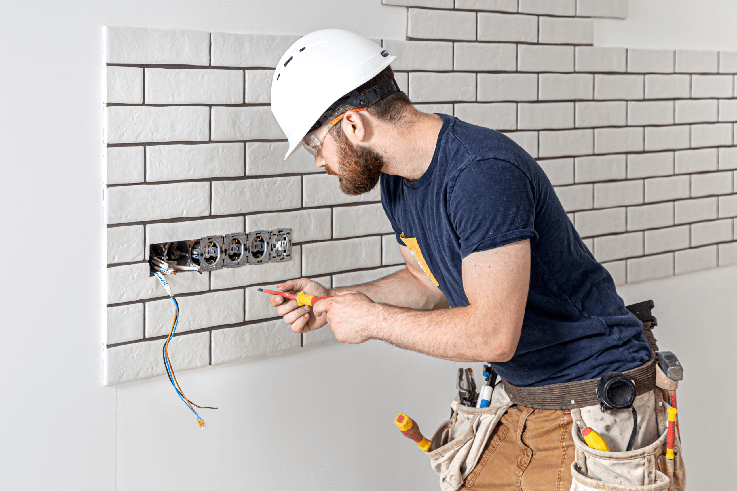 Electrician construction worker with a beard in overalls during the installation of sockets. Home renovation concept.